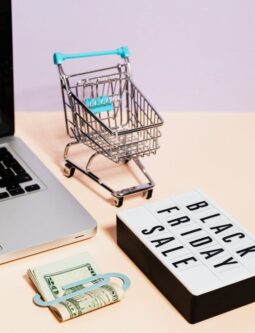 Image of a laptop, mini cart, cash, and Black Friday sale sign representing online shopping deals.